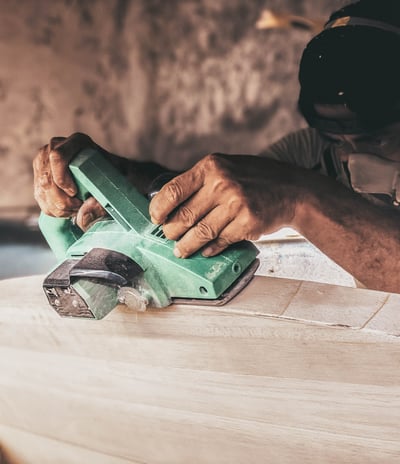 Craftsman shaping a handmade balsa surfboard with an electric planer