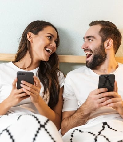 a man and woman sitting on a bed with their cell phones with foodax