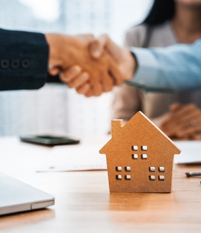 A handshake between two professionals over a signed real estate contract, symbolizing success