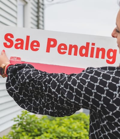 "A real estate agent placing a 'Sale Pending' sign in front of a home, symbolizing a successful sale