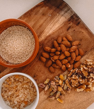 A wooden cutting board topped with a variety of raw nuts used in traditional Panjeeri preparation.