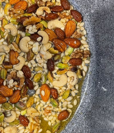 A pan of assorted nuts frying in desi ghee, the base preparation for traditional Panjeeri