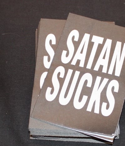Free handouts at biker ministry table says “Satan Sucks.”