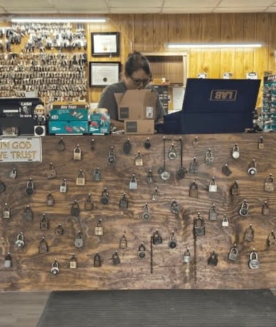 Emily, a female locksmith, assisting customers at the front counter of Jack's Locksmith in Burnsville, NC, wall of locks