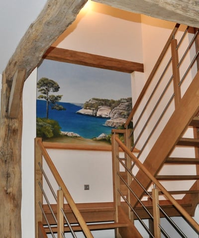 Une ouverture en trompe-l'oeil dans une cage d'escalier, invite au voyage en bord de mer. Le faux bois intègre l'ensemble.