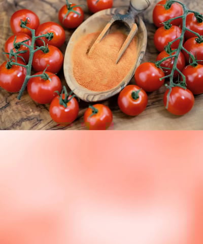 Bright red tomato powder in a wooden bowl with fresh tomatoes in the background