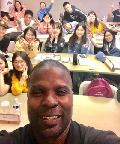 Dr. Marlon Ware standing in front of his class with students holding up the peace sign