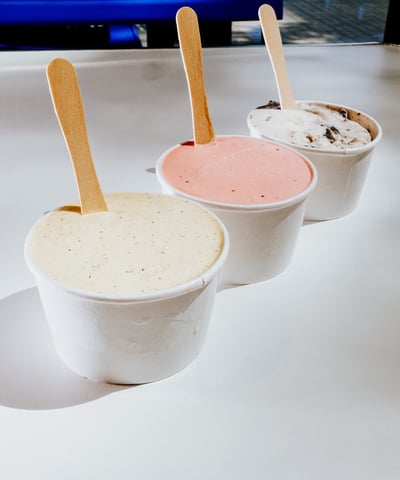 Tres tarrinas de helado de Flipa con sabores variados (vainilla, fresa y oreo) sobre mesa blanca.