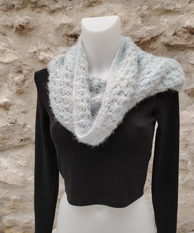 Tour de cou tricoté à la main posé sur un mannequin blanc habillé d'un haut noir