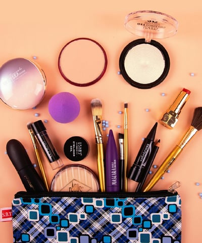 oranje achtergrond met op de voorgrond penselen , kwasten, lippenstift, blusher, mascara, sponsjes