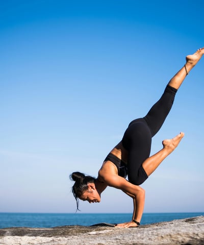 er is een vrouw te zien die yoga uitoefent met op de achtergrond de zee en blauwe lucht