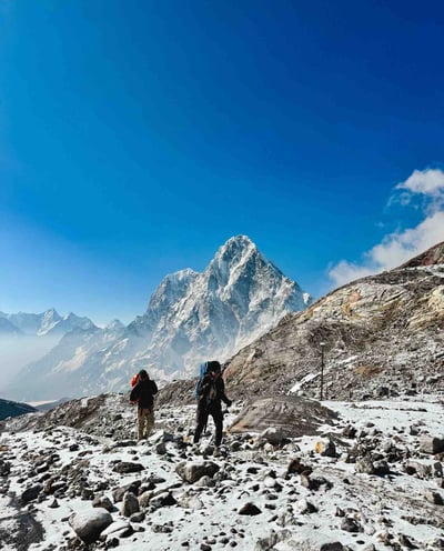 Manon and her Nepali guide walking with the snow-covered peak of Taboche in the background.