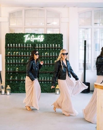  Bridesmaids walking past the grass champagne walls behind them.