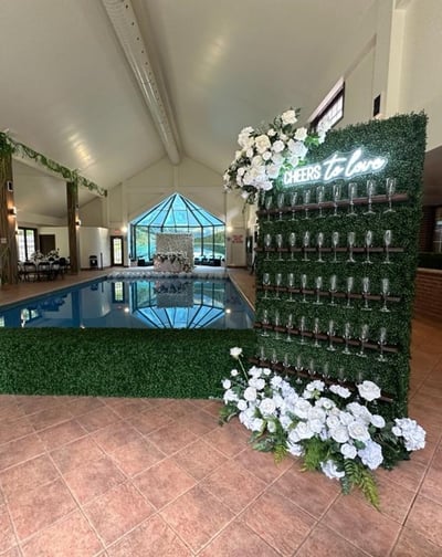 Wedding champagne wall set up with a cheers to love neon with white roses and greenery