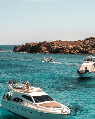 Boats floating on clear blue sea near rocky coast.