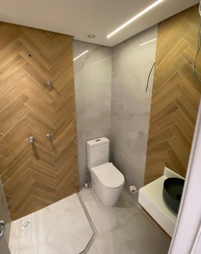 Banheiro reformado pela Nattú Engenharia com porcelanato claro e madeira em estilo espinha de peixe