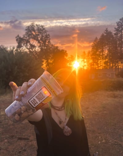 a woman with green hair holding a cup of rocks. by the sunset
