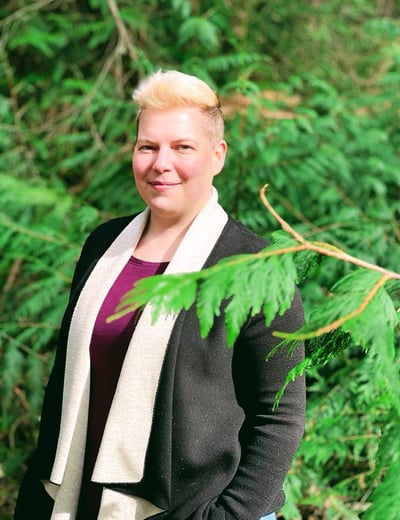 A woman in a black cardigan and jeans standing in front of trees