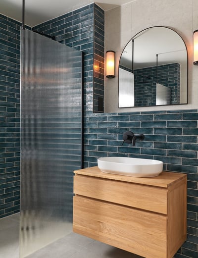 deep, glossy teal metro tiles, laid in a horizontal stack with white grout and oak floating vanity