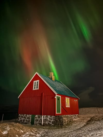 "Red house in the snowy Faroe Islands under vibrant northern lights in green, red, and orange hues."