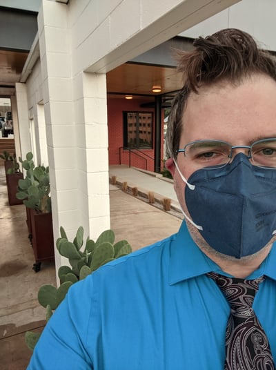 photo of GJ, 40-something white person dressed semi-professionally, standing in front of a row of cactuses and pillars.