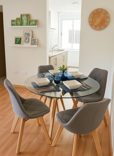 Comedor de departamento muestra con mesa redonda de cristal, sillas tapizadas en gris, decoración