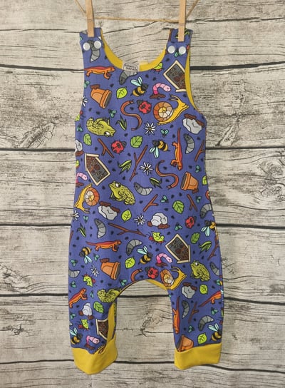 a baby's overalls with a blue and yellow romper with garden creatures forest school print