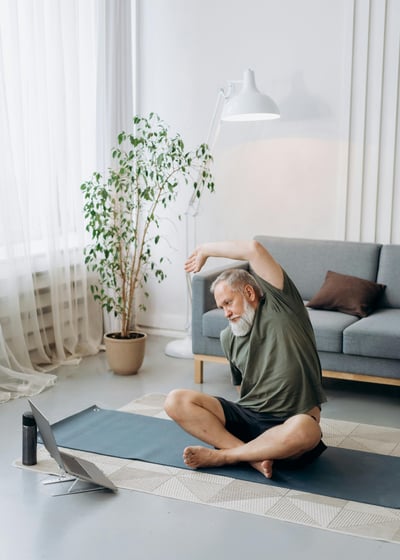 Hombre adulto mayor con barba blanca meditando con las manos en posición de oración frente a una laptop abierta sobre una est