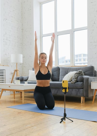 Mujer joven sentada sobre un tapete de yoga en su sala de estar, estirando los br