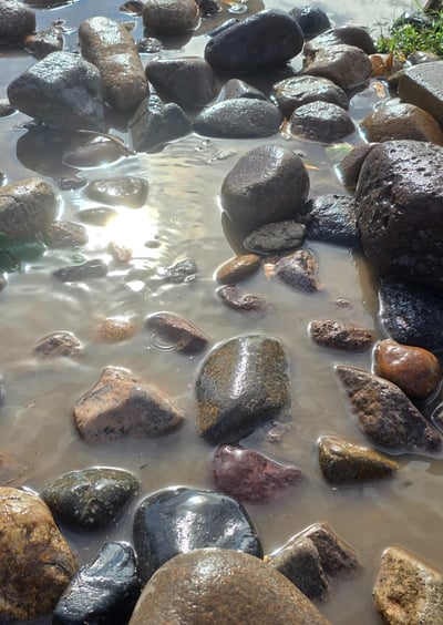 water glistens in the sun with colorful rocks in a pool 