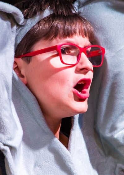 Child wearing an elephant costume with large ears and red glasses, performing expressively on stage