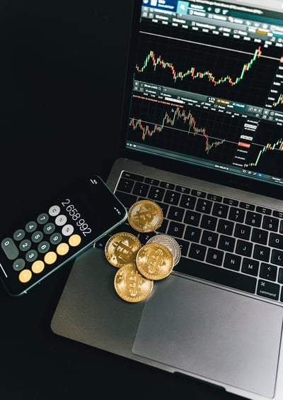 Cryptocurrency coins and smartphone calculator on a laptop showing Bitcoin trading charts.