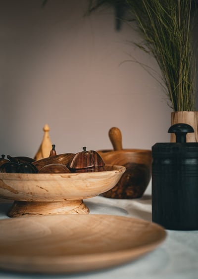 Objets artisanaux en bois posés sur une table : plat en bois clair sur pied rempli de fruits décorat