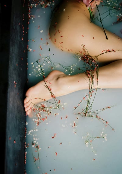 Bare legs in a bath with floating flowers and herbs