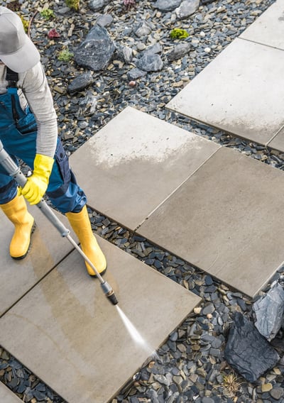 A man in blue clothes pressure washing some large stones