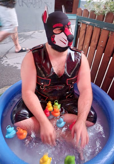 A man playing in a kiddie pool wearing a pup mask.