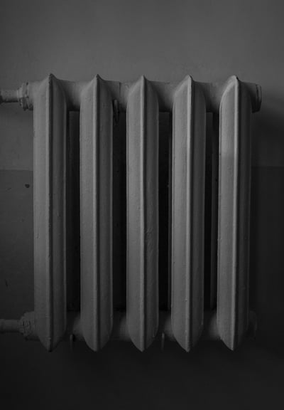 Monochrome image of a cast iron radiator against a wall.