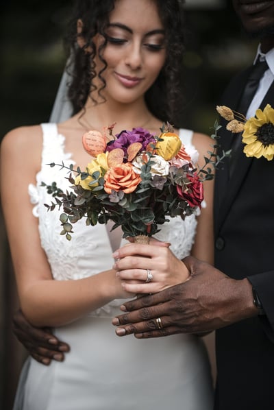 A Hertfordshire bride in a white dress holding a bouquet of paper flowers, standing outdoors.