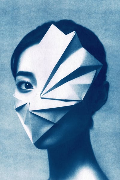 Close-up of a woman with dark hair, smooth skin, and one visible expressive eye. A geometric paper m