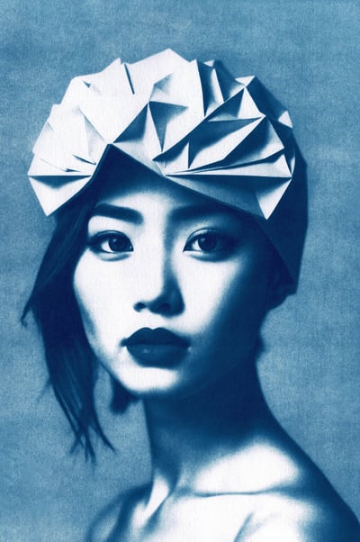 Close-up of a woman with blue-toned skin, dark eyebrows, and full lips, wearing a geometric paper he