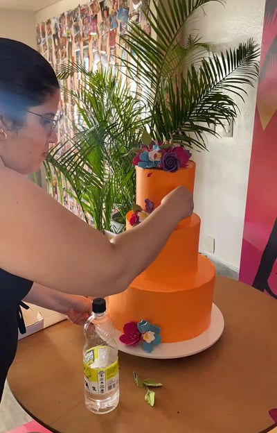 Mulher trabalhando em um bolo de aniversário laranja decorado com flores em um ambiente festivo. A c