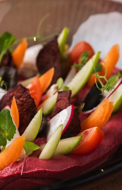 Ensalada colorida con hummus de remolacha, crudités frescos y falafel, servida en un bol artesanal.
