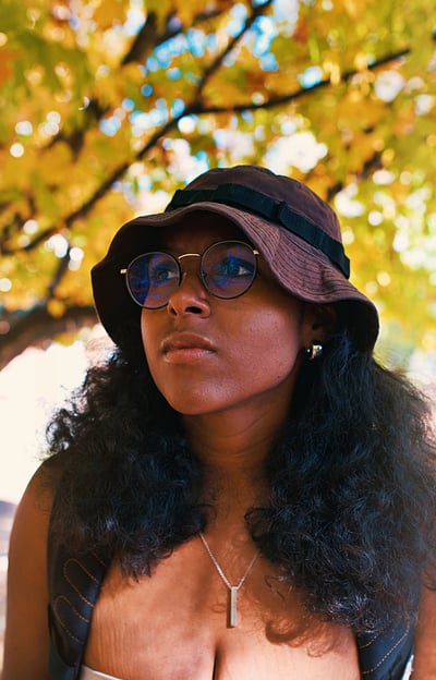 Young college black woman birdwatching underneath golden yellow autumn trees.