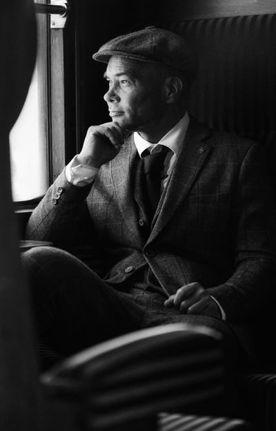 a man in a suit and hat sitting on a chair fashion shoot peaky blinders