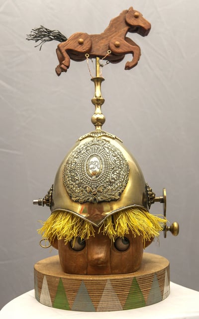 Model of a child's head wearing a shiny guard's helmet topped by a galloping horse