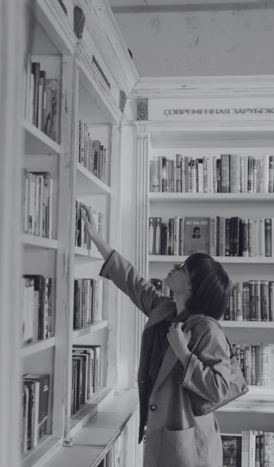 Young woman browsing books in a cozy London bookshop, carefully selecting a novel from a shelf