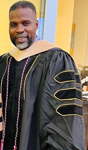 Dr. Marlon Ware standing and smiling in his graduation gown