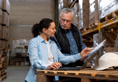 a man and woman in a warehouse setting checking files