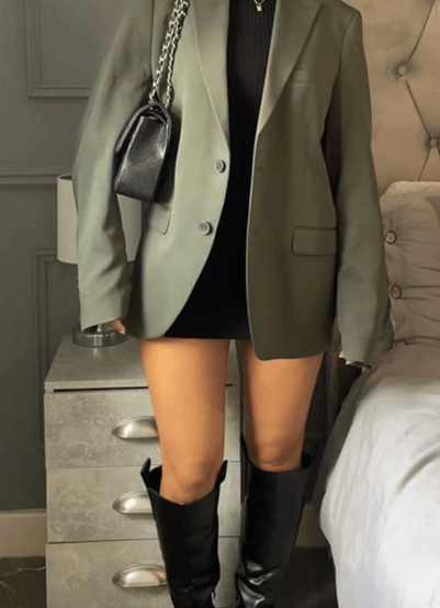 a woman in a black dress and boots is standing in front of a bed