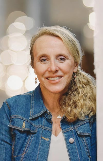 Owner Chris Bisner smiles while leaning against a wall in a jean jacket, blonde hair, and smile